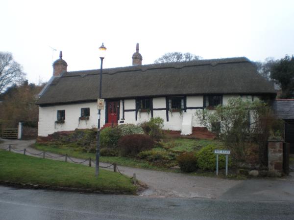 Pair of cottages, now single dwelling. C17 or earlier, with extensive later alterations; altered further in late C20. Part timber and cruck framed, with brick nogging; part sandstone; all now whitewashed and rendered; thatched roof with whitewashed stacks.  EXTERIOR: single storey, 5 bays, built on a sloping outcrop of rock with ten steps up to the front entrance. Eight panels of large square framing are exposed to right of front door. Front door is 4-panelled with glazed upper panels. Windows are horizontal sliding sashes with glazing bars, two to left of front door, four to right of door, set in alternate panels above mid-rail.  INTERIOR: timber-frame incorporates cruck trusses in partition walls of the bedroom and present bathroom, and on the line of the firebeam to the living room. Old doors and exposed ceiling timbers throughout 